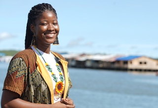 Imagen de mujer joven afro, lleva un collar con un girasol que resalta en su sonrisa, está frente a bahía en Buenaventura
