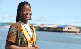 Imagen de mujer joven afro, lleva un collar con un girasol que resalta en su sonrisa, está frente a bahía en Buenaventura