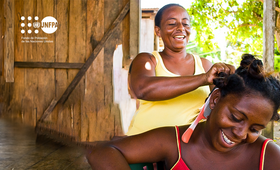 Una mujer afrocolombiana peina a otra mujer afro, están sonrientes