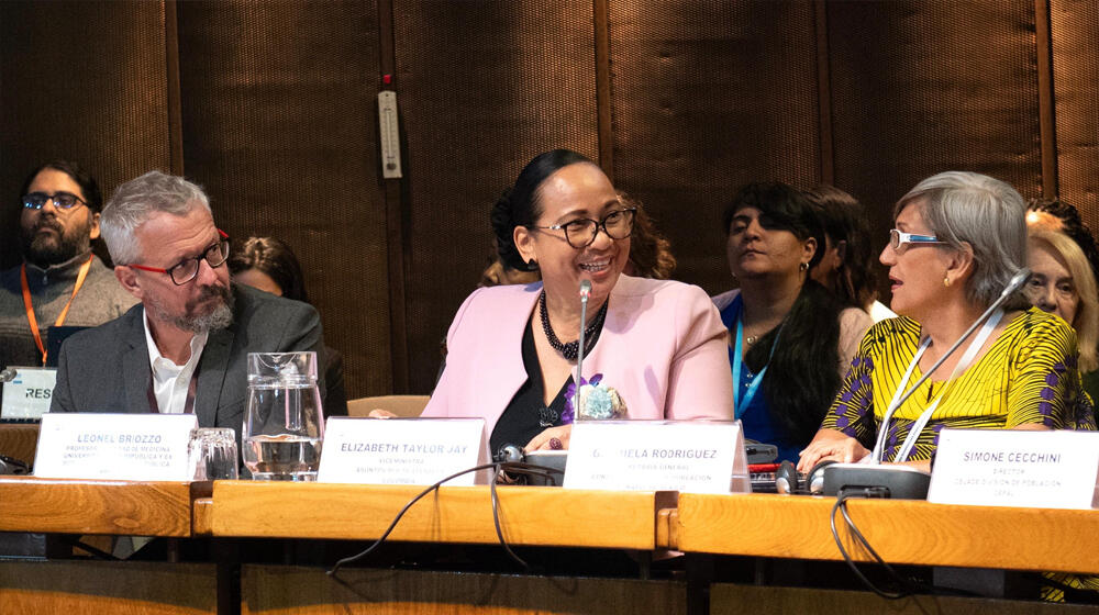 Dos mujeres y un hombre conversando en una mesa del recinto de la Conferencia sobre Población y Desarrollo 2023